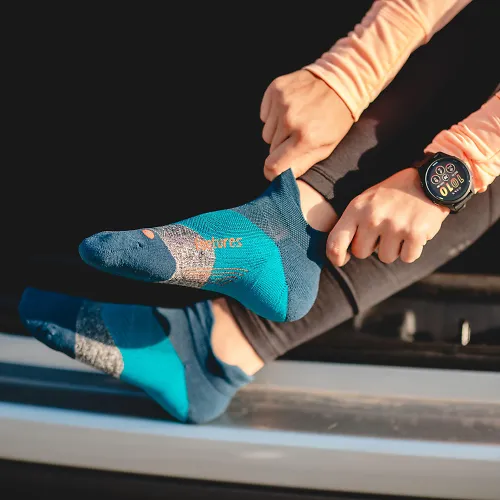 A woman sits on her car, sliding on a pair of Feetures socks.